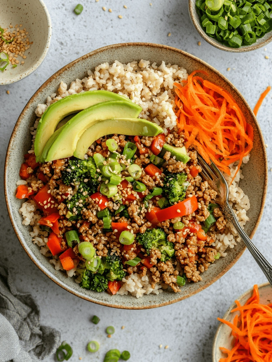 Overhead view of a Teriyaki Turkey Rice Bowl with avocado slices, shredded carrots, green onions, broccoli, and red bell peppers served over brown rice.