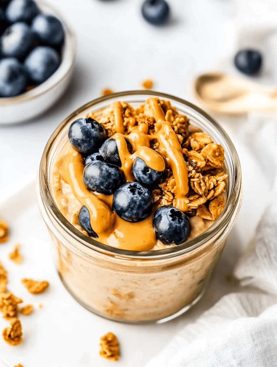 Blended overnight oats in a glass jar topped with fresh blueberries, granola, and creamy nut butter