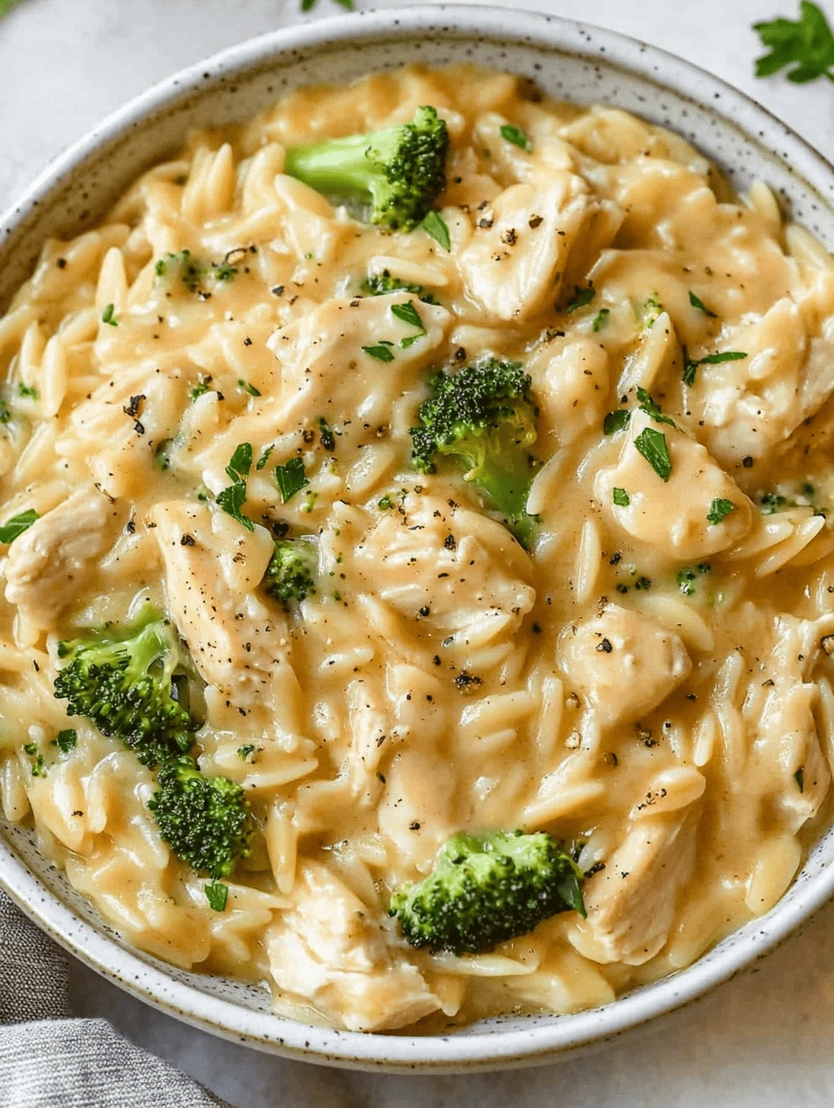Close-up of creamy chicken broccoli orzo pasta with cheese and green herb garnish in a white bowl.