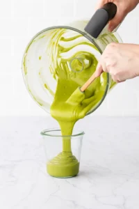 Pouring finished pistachio butter into a glass jar for pistachio butter recipe